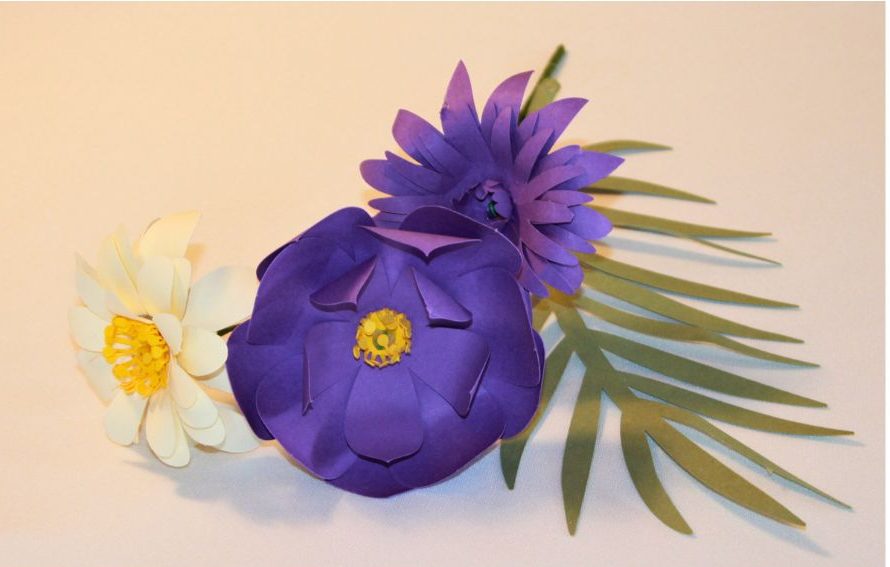 Composition florale en papier : deux fleurs aux tons violet, sublimées par une fleur beige au coeur jaune.