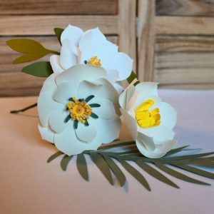 Bouquet de trois fleurs en papier blanc avec étamines jaunes et feuillage vert.